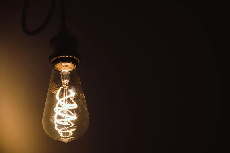 A lit incandescent bulb with a spiral filament against a dark background.