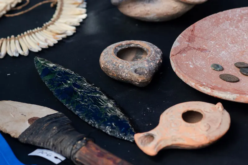 A dark chipped-stone blade beside ceramic oil lamps and shell ornaments on a display table.