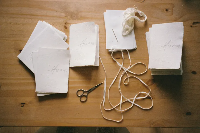 White sheets of handmade paper on a wooden table, beside twine and scissors.