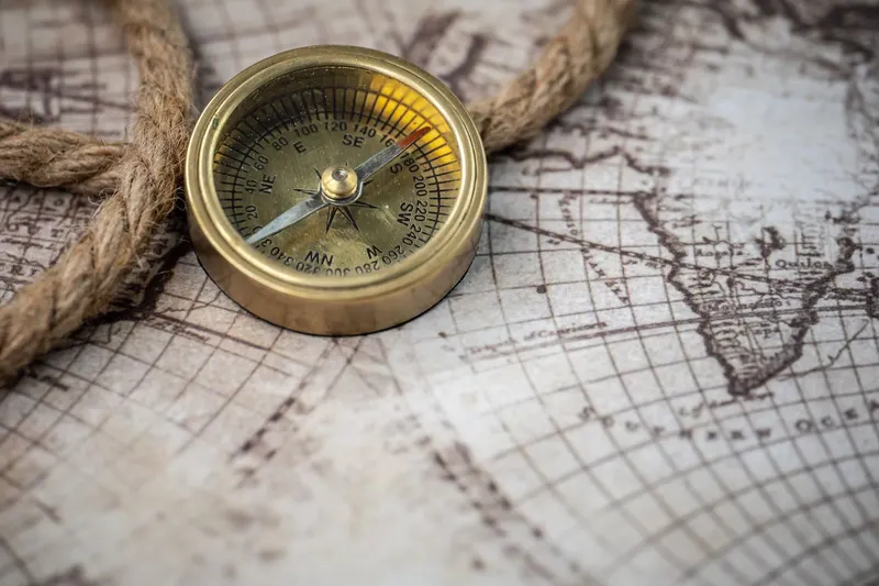 A brass compass lying on an old world map beside a length of rope.