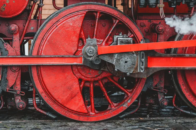 Large red driving wheels and connecting rods of a steam locomotive.