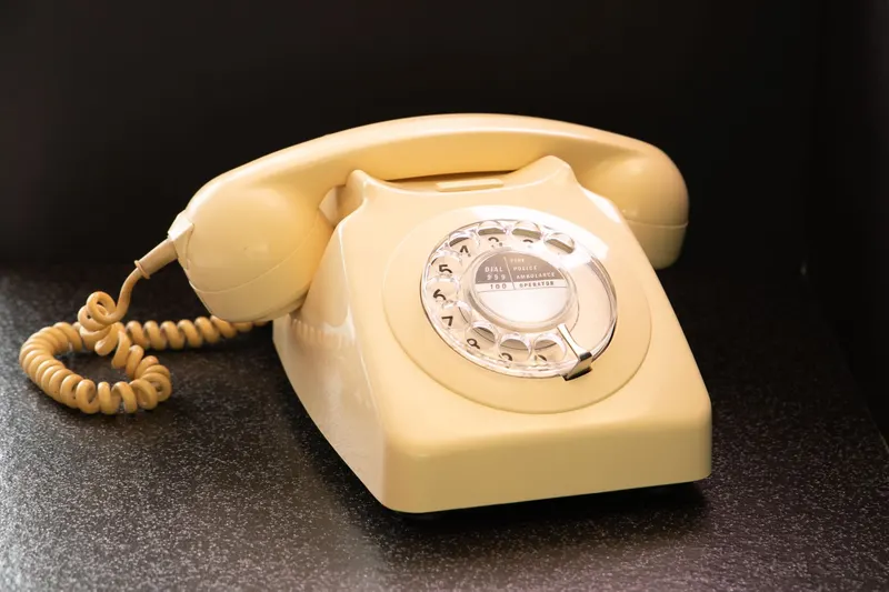 A cream-colored rotary telephone with a coiled cord on a dark surface.