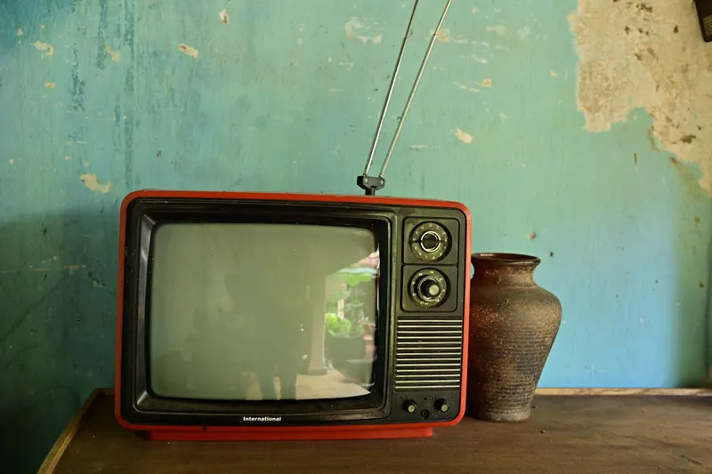 An old tube television with an indoor antenna in front of a greenish wall.