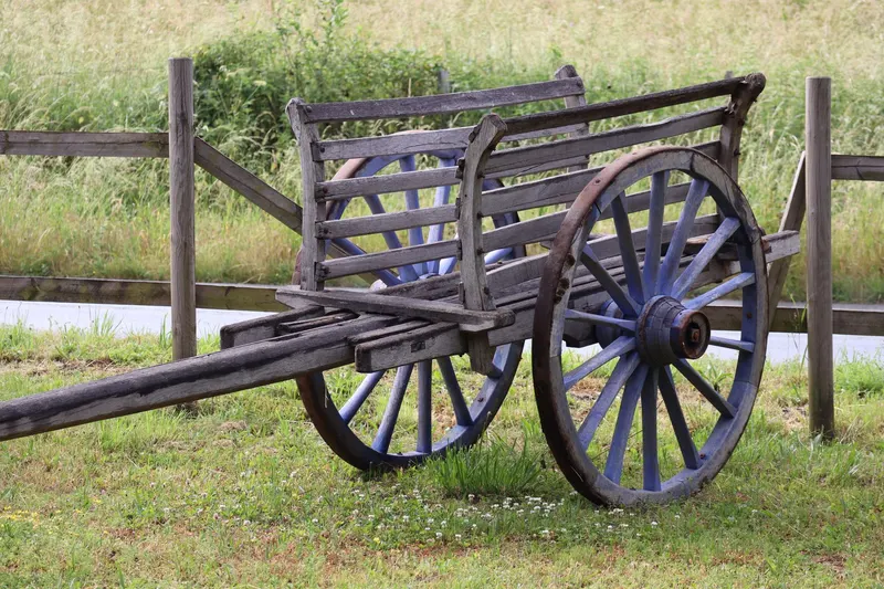 An old wooden cart with spoked wheels parked in a grassy field.