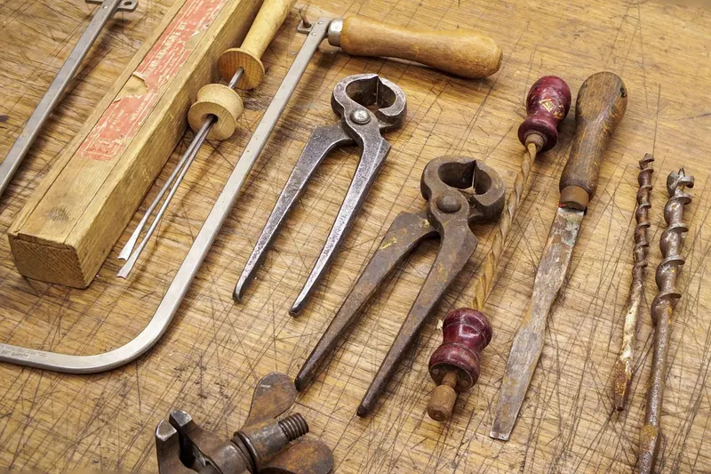 Old hand tools, including pliers, drill bits, files, and chisels, laid out on a wooden surface.
